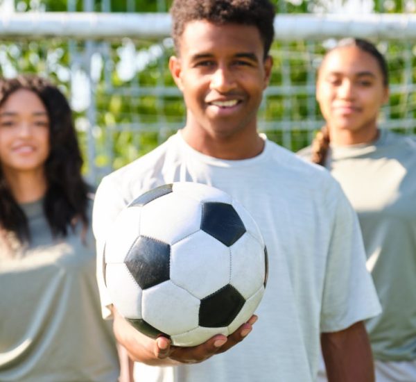 Young soccer player holding a ball with teammates in background Young soccer player holding a ball with teammates in background